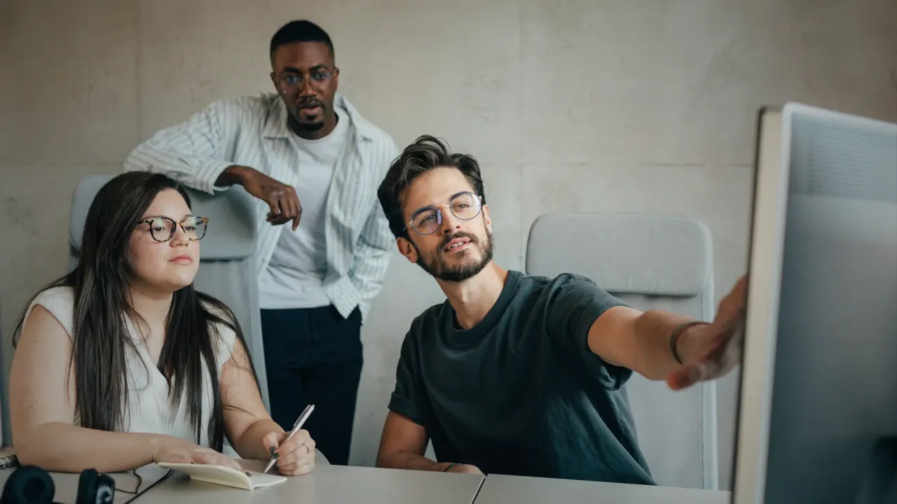 Junges Team aus drei Personen, die über etwas am Bildschirm sprechen