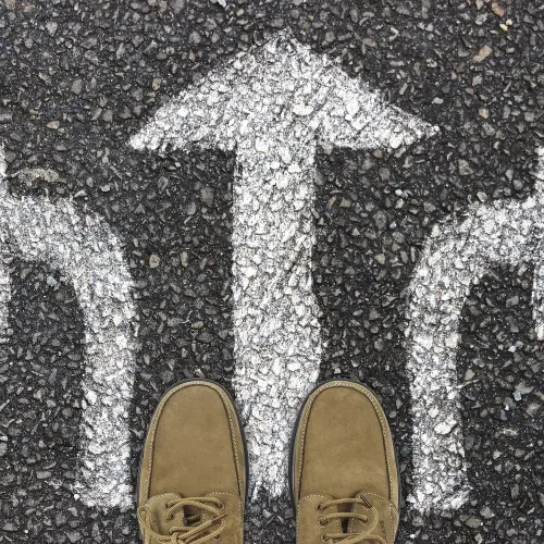 Schuhe vor drei auf Asphalt gemalten Pfeilen in verschiedene Richtungen als Sinnbild für die Wahl der passenden Projektmanagement Methode